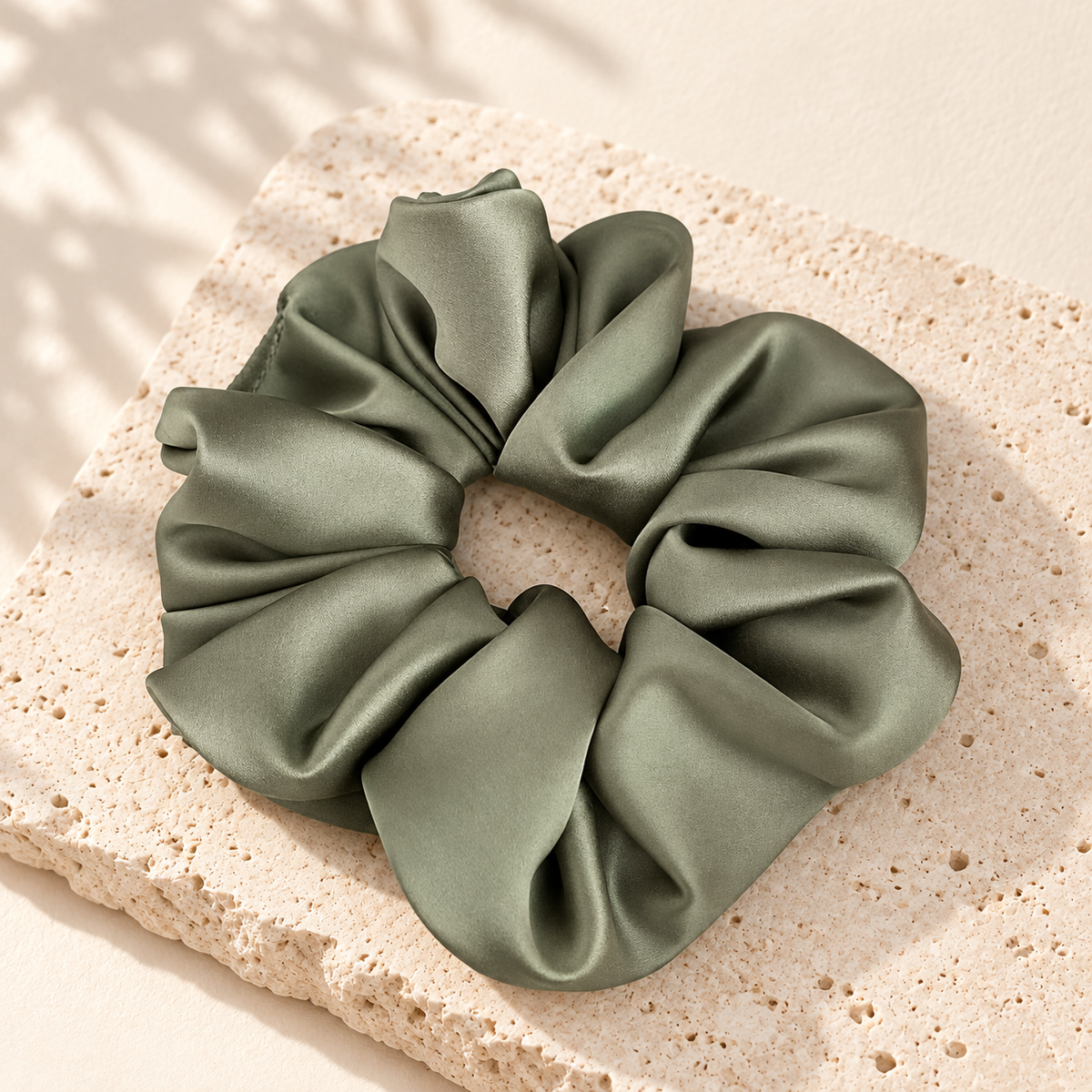 Scrunchie géant en satin vert sauge, posé sur une pierre claire.