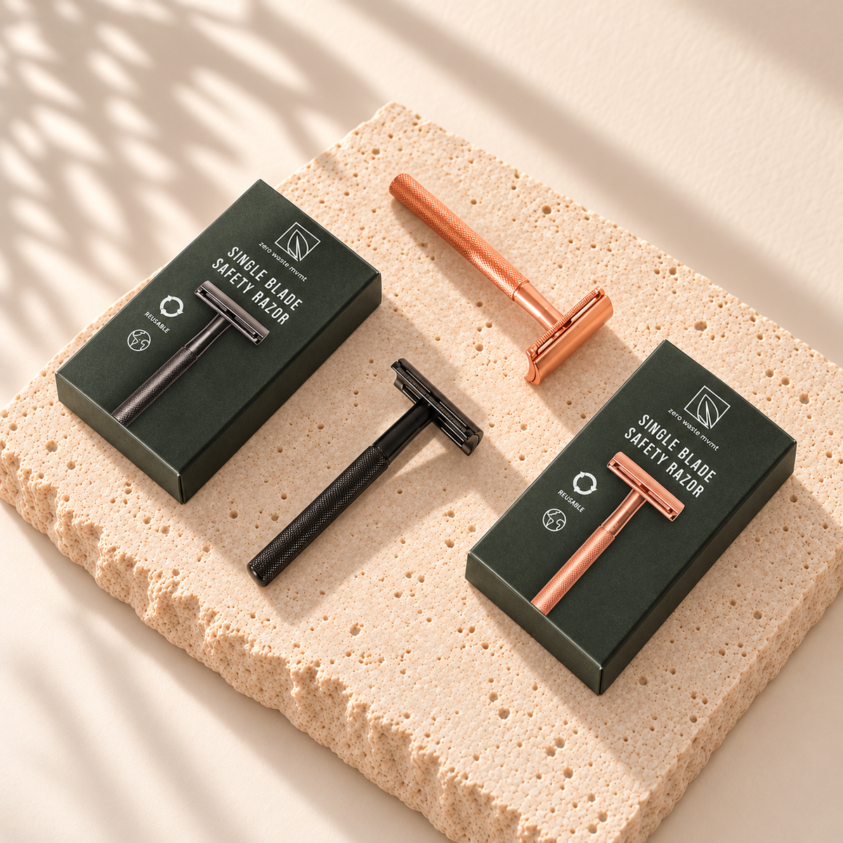 Rasoirs noir et rose doré Zero Waste MVMT avec leurs boîtes marquées, posés sur une pierre claire.