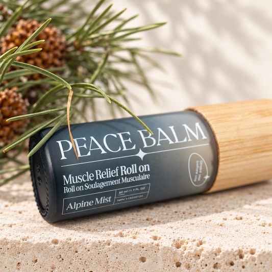 Peace Balm Alpine Mist fermé, couché sur une pierre claire auprès de branches de pin.