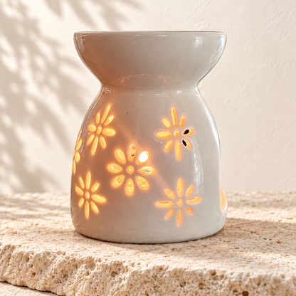Diffuseur en céramique blanc allumé, à motifs floraux, posé sur une pierre claire.
