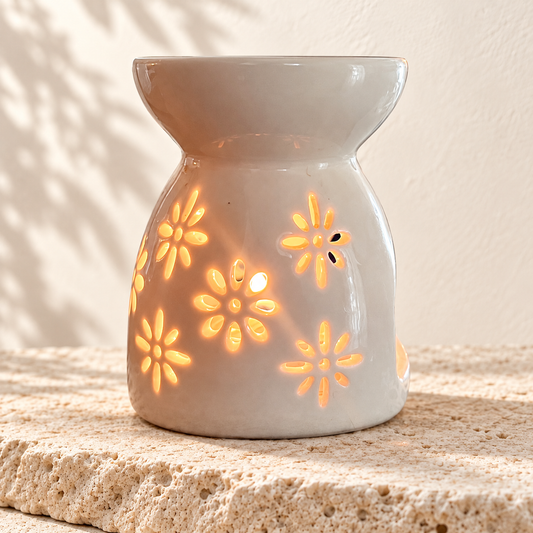 Diffuseur en céramique blanc allumé, à motifs floraux, posé sur une pierre claire.