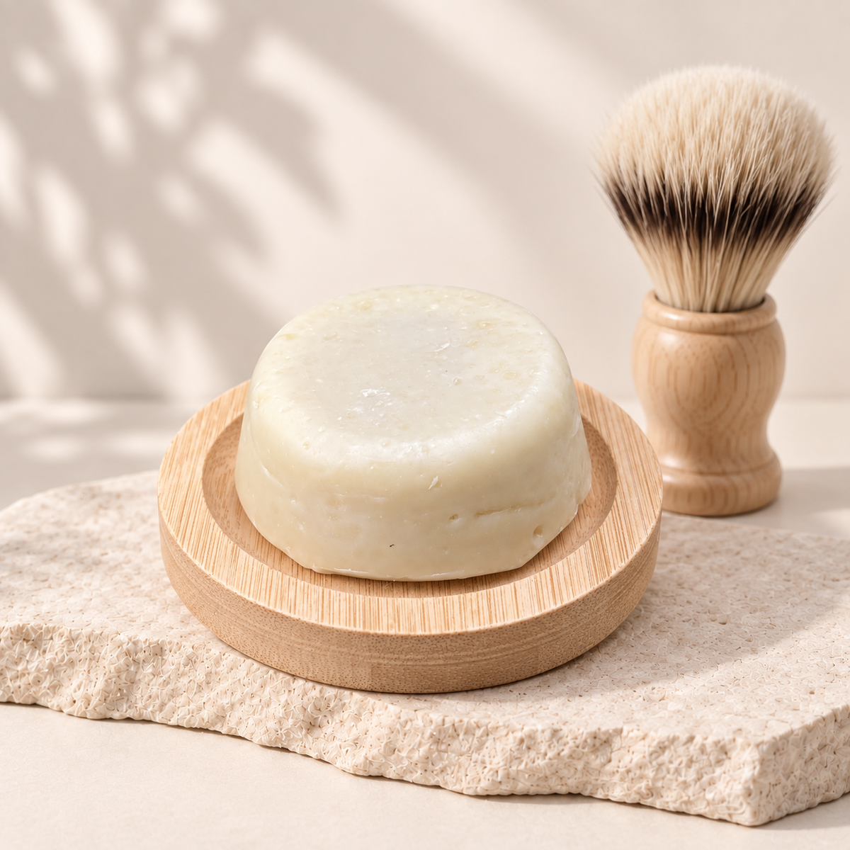 Crème à raser naturelle blanche ronde sur porte-savon en bois clair avec un blaireau à manche bois à poils doux.
