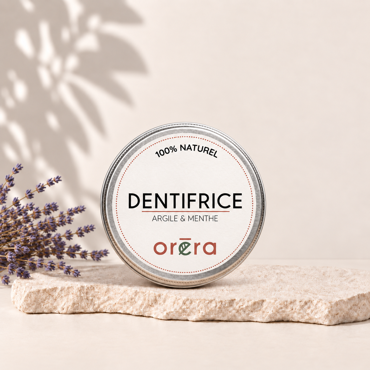 Dentifrice naturel à l'argile et menthe dans pot rond blanc posé sur pierre beige avec ombre feuillage.