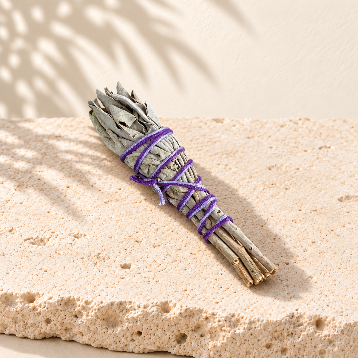 Mini bâton de sauge blanche au fil violet, couché sur une dalle de pierre claire.