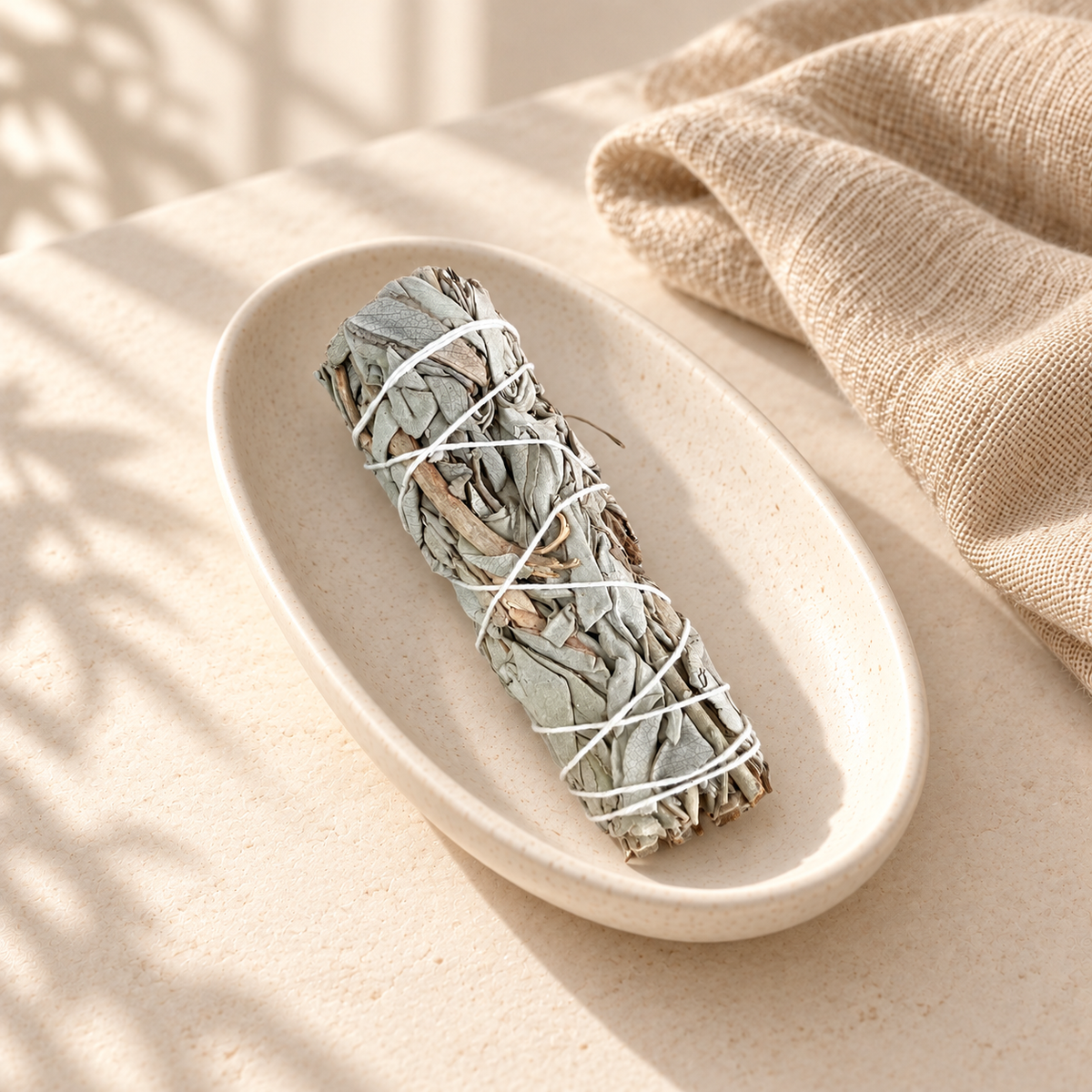 Bâton de sauge blanche de Californie, non allumé, dans une coupelle en céramique ivoire avec du lin beige.