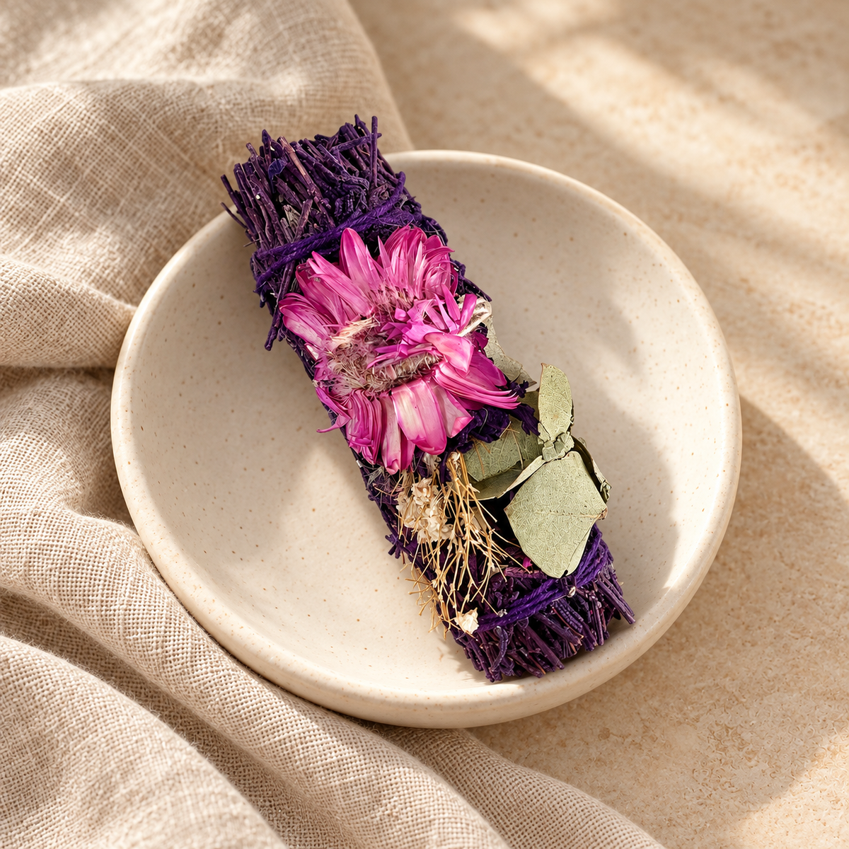 Bâton de sauge lavande et fleurs séchées, non allumé, dans une coupelle en céramique ivoire avec du lin beige.