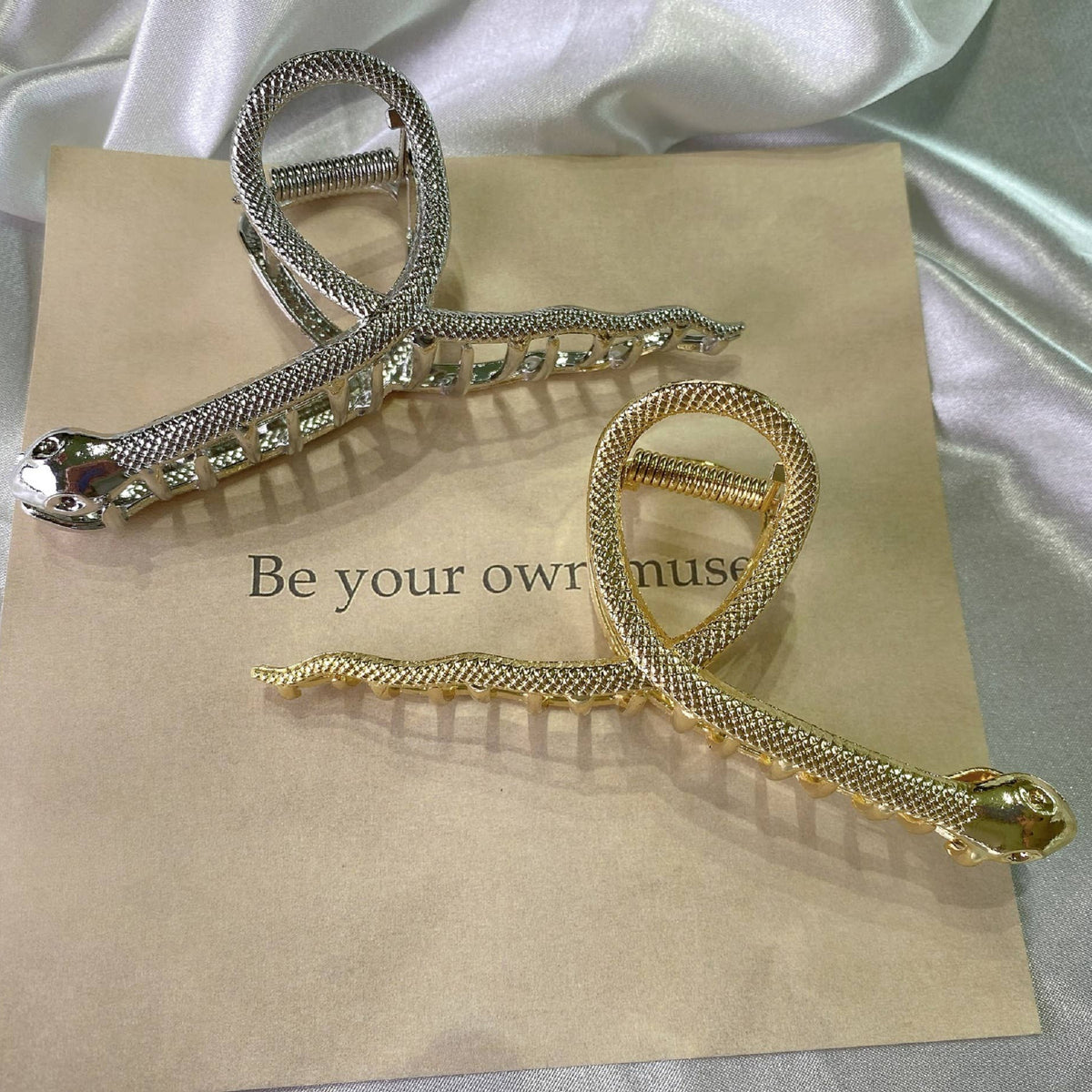 Pinces à cheveux dorée et argentée en forme de serpents entrelacés.
