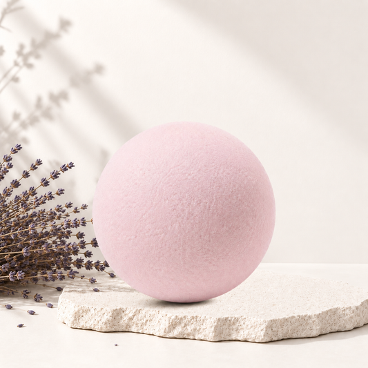Bombe de bain sphérique rose pâle posée sur une pierre texturée avec branche de lavande sèche à côté.