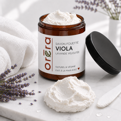 Pot en verre brun avec étiquette blanche, crème fouettée blanche, parfum lavande veloutée, couvercle noir posé à côté.