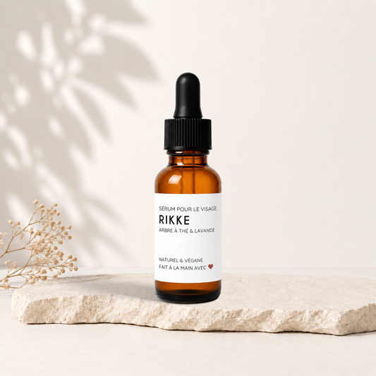 Sérum visage RIKKE en flacon ambré avec pipette noire, étiquette blanche minimaliste, posé sur pierre beige.