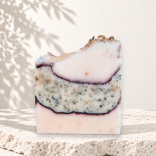 Savon artisanal beige avec couches texturées vertes et violettes, exfoliant naturel au lait de chèvre.
