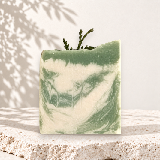 Savon carré vert et blanc marbré au lait de chèvre avec branche décorative, style artisanal.